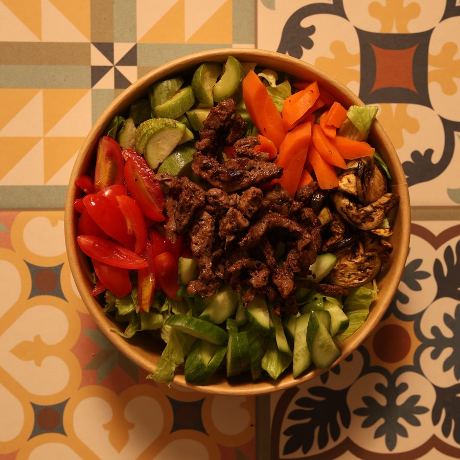 Salad bowl with grilled beef strips, peppers, carrots and greens
